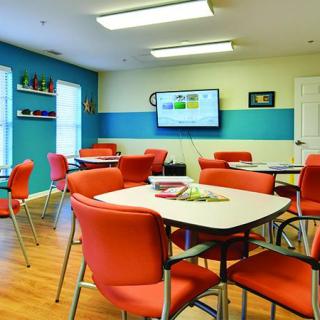 A brightly colored classroom with red chairs, tables, and a television on the wall.