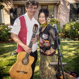 A musical duo performing outdoors with a guitar and microphone.