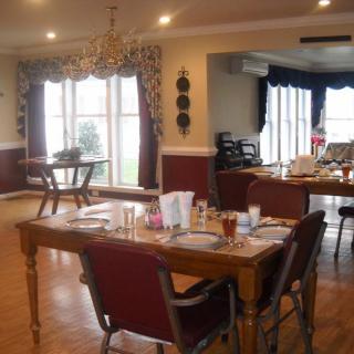 A well-lit dining room with set tables and a chandelier, featuring large windows and decorative curtains.