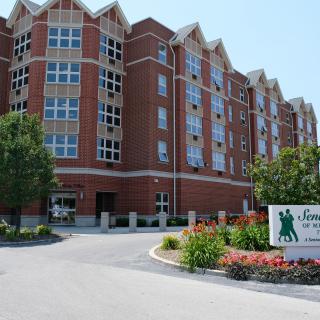 A multi-story brick residential building with landscaping at the entrance.