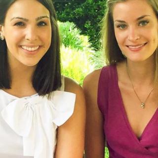 Two women smiling outdoors while sitting together.