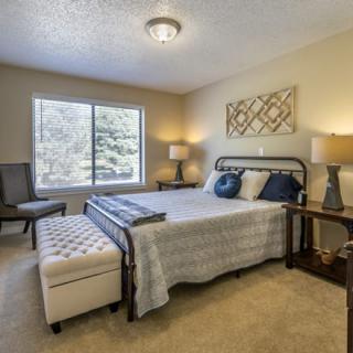 A cozy bedroom with a double bed, bedside tables, and lamps, featuring a large window and neutral decor.