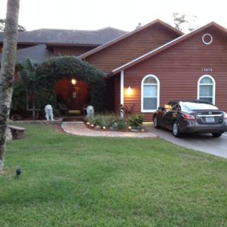 A suburban house with a neatly maintained lawn and garden, featuring a car parked in the driveway during the evening.