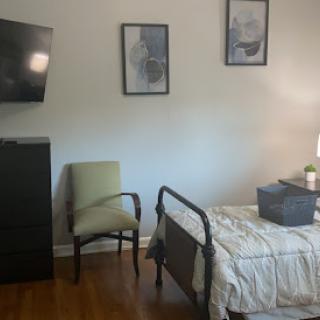 A cozy bedroom featuring a hospital bed, armchair, TV, and decorative artwork.