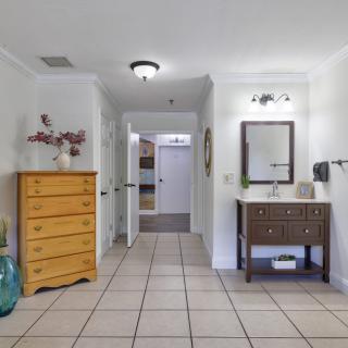 A hallway with a dresser on the left and a sink with a mirror on the right, featuring tile flooring.