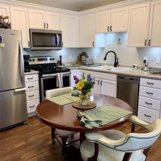 A modern kitchen with stainless steel appliances, white cabinets, and a cozy dining area featuring a round wooden table with chairs and a floral centerpiece.