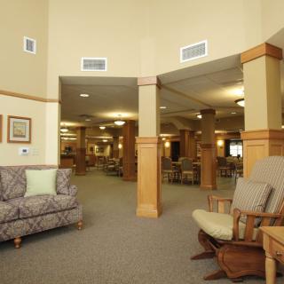 A spacious lobby area featuring comfortable seating with sofas and rocking chairs, surrounded by columns and well-lit with ceiling lights.