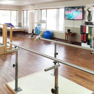 A physical therapy room equipped with parallel bars and various exercise equipment.