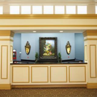 A well-lit reception area with classic decor, featuring a central artwork and two ornate wall sconces.
