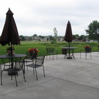 An outdoor patio with tables, chairs, and umbrellas overlooking a grassy area.