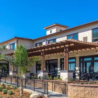 A modern building with a wooden pergola and outdoor seating on a sunny day.