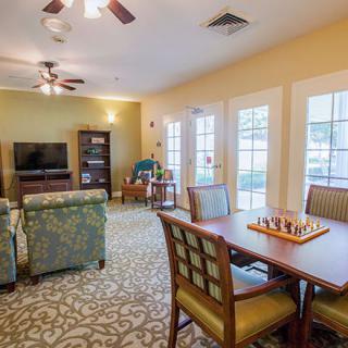 A cozy living room with a chess board on the table, sofas facing a TV, and large windows letting in natural light.
