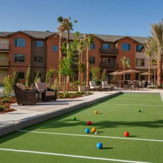 A well-maintained bocce court adjacent to a residential building with patio seating and lush landscaping.
