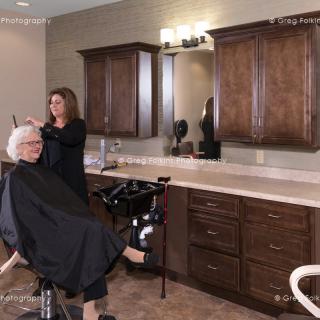 A hairstylist is giving a haircut to a senior woman in a well-furnished salon.