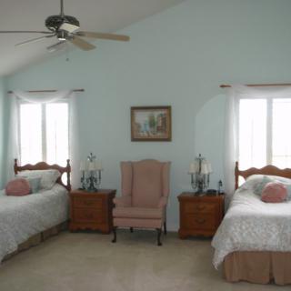 A cozy bedroom with twin beds, pastel decor, and a ceiling fan.