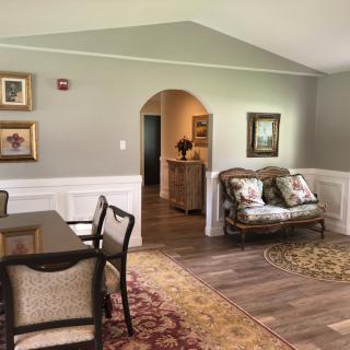 A cozy living room and dining area featuring classic furniture, decorative paintings, and warm lighting.