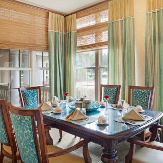 A beautifully set dining table in a well-lit room with elegant curtains and wooden chairs.