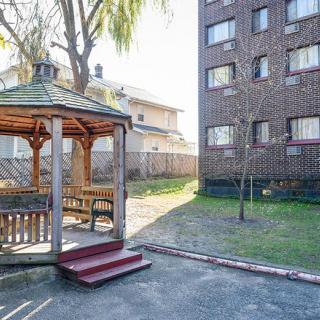A small yard with a wooden gazebo next to an apartment building.