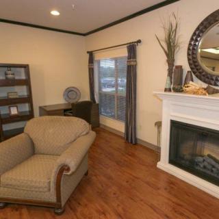 A cozy living room with a fireplace, armchair, bookshelf, and wooden flooring.