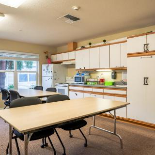 A shared kitchen and dining area with tables, chairs, and appliances.