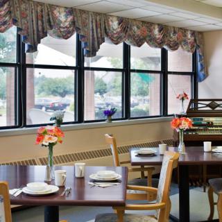 A cozy dining area with tables set by the windows, adorned with vases of flowers.