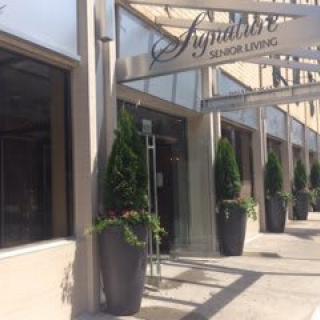 Exterior view of a shop with signage and large potted plants along the sidewalk.