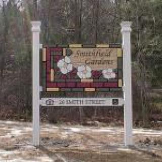 A wooden sign for a garden, located outdoors amidst trees.