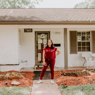 A woman standing in front of a house, posing confidently.