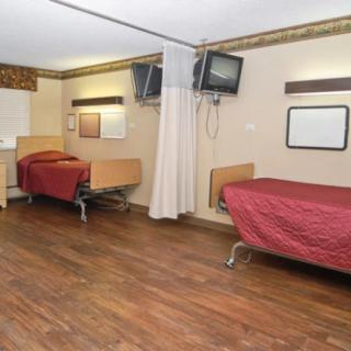 A hospital room with two beds, televisions, and a wooden floor.