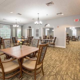 A spacious dining area with multiple tables and chairs, featuring bright lighting and a carpeted floor.