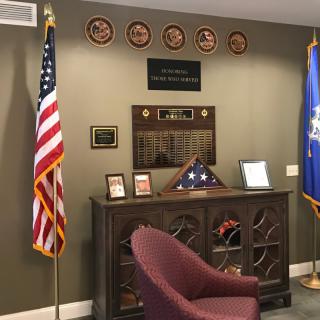 An office space adorned with military memorabilia, featuring flags, plaques, and a display case.
