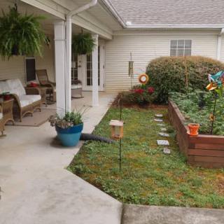 A cozy backyard patio with seating and a raised garden bed filled with plants.