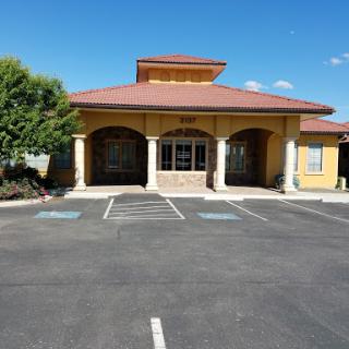 A commercial building with a welcoming entrance and ample parking, set against a clear blue sky.