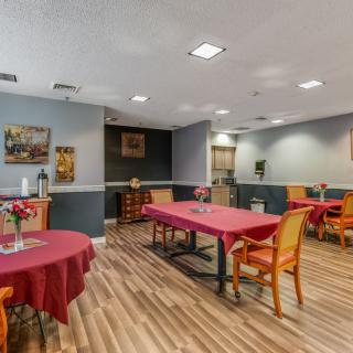 A cozy dining room with neatly arranged tables and chairs, featuring warm lighting and a wooden floor.
