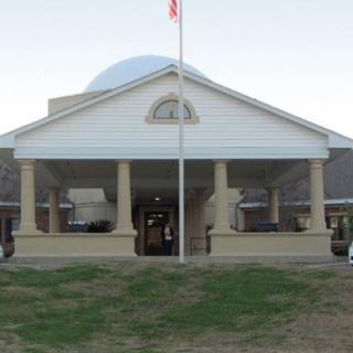A building with a dome and pillars at the entrance, featuring a flagpole in front.
