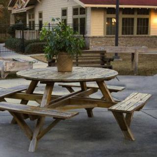 A round wooden picnic table with attached benches, placed on a patio with a potted plant on top.