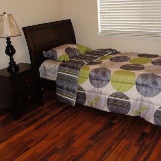 A tidy bedroom with a single bed, nightstand, and lamp on a hardwood floor.