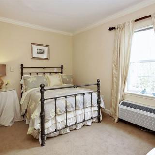 A cozy bedroom with a traditional iron bed frame, soft neutral tones, and ample natural light from a large window.