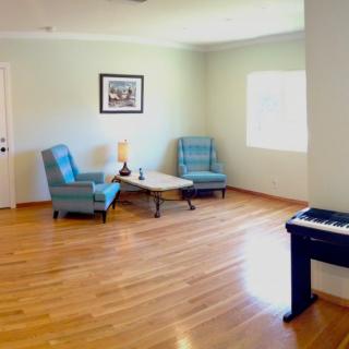 A spacious living room with wood flooring, featuring two armchairs, a coffee table, and a keyboard piano.
