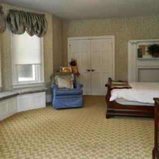 A cozy bedroom featuring a large bed, blue armchair, and patterned carpet with natural light coming through the windows.