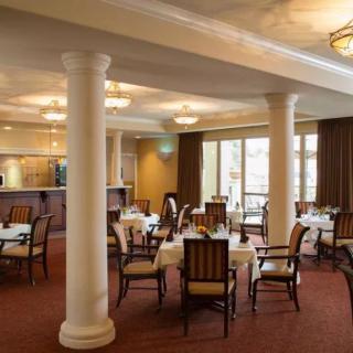 A cozy restaurant dining area with elegantly set tables and chairs, surrounded by ornate columns and warm lighting.
