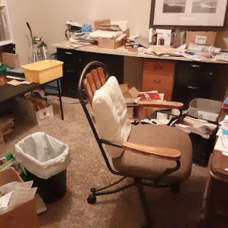 A cluttered home office filled with papers and other items, showcasing a disorganized workspace.