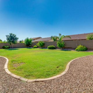 A well-maintained backyard with a green lawn surrounded by trees and shrubs under a clear blue sky.