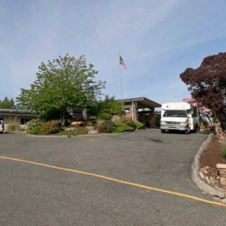 A parking lot with an RV parked near a building, surrounded by trees and a flagpole.