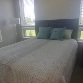 A cozy bedroom with a neatly made bed and decorative pillows, illuminated by natural light from surrounding windows.