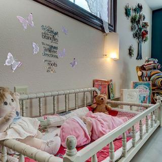 A cozy child's room with a bed adorned in pink bedding, featuring stuffed animals and butterfly wall decorations.