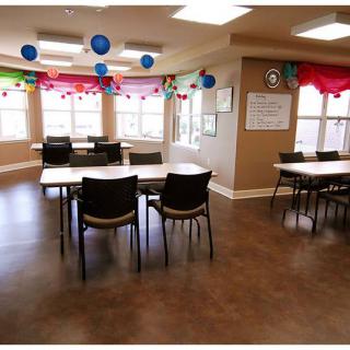 A decorated classroom with tables and chairs, featuring colorful balloons hanging from the ceiling.