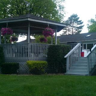 A quaint gazebo with a deck, surrounded by lush greenery and hanging flowers.