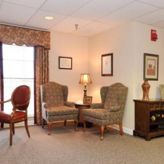 A cozy living room with comfortable armchairs, a lamp, and framed artwork on the walls.