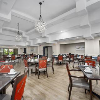 A spacious and elegant restaurant dining area with red chairs and wooden tables under modern chandeliers.